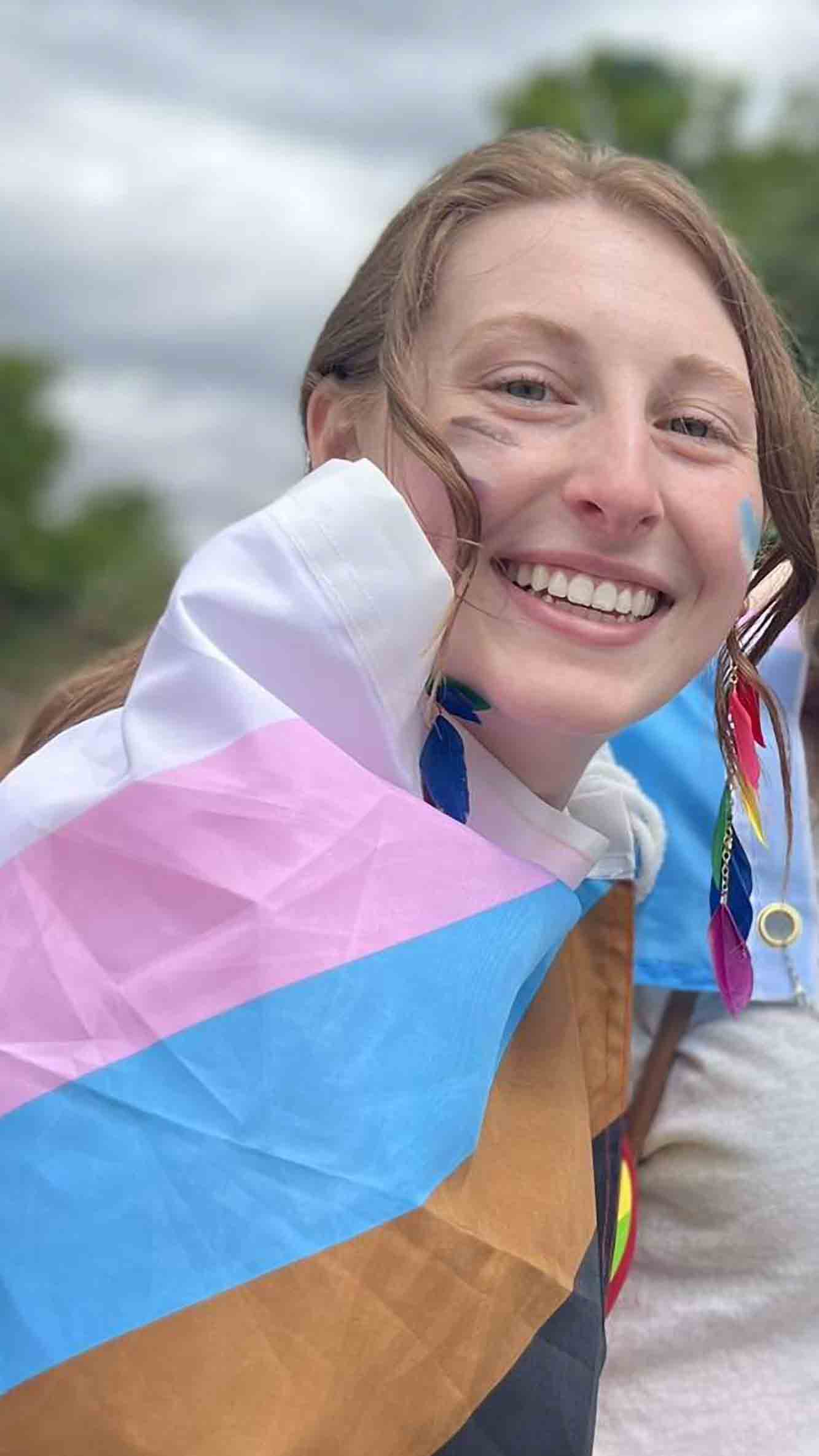 a young white woman is smiling at the camera, wrapped in a pride