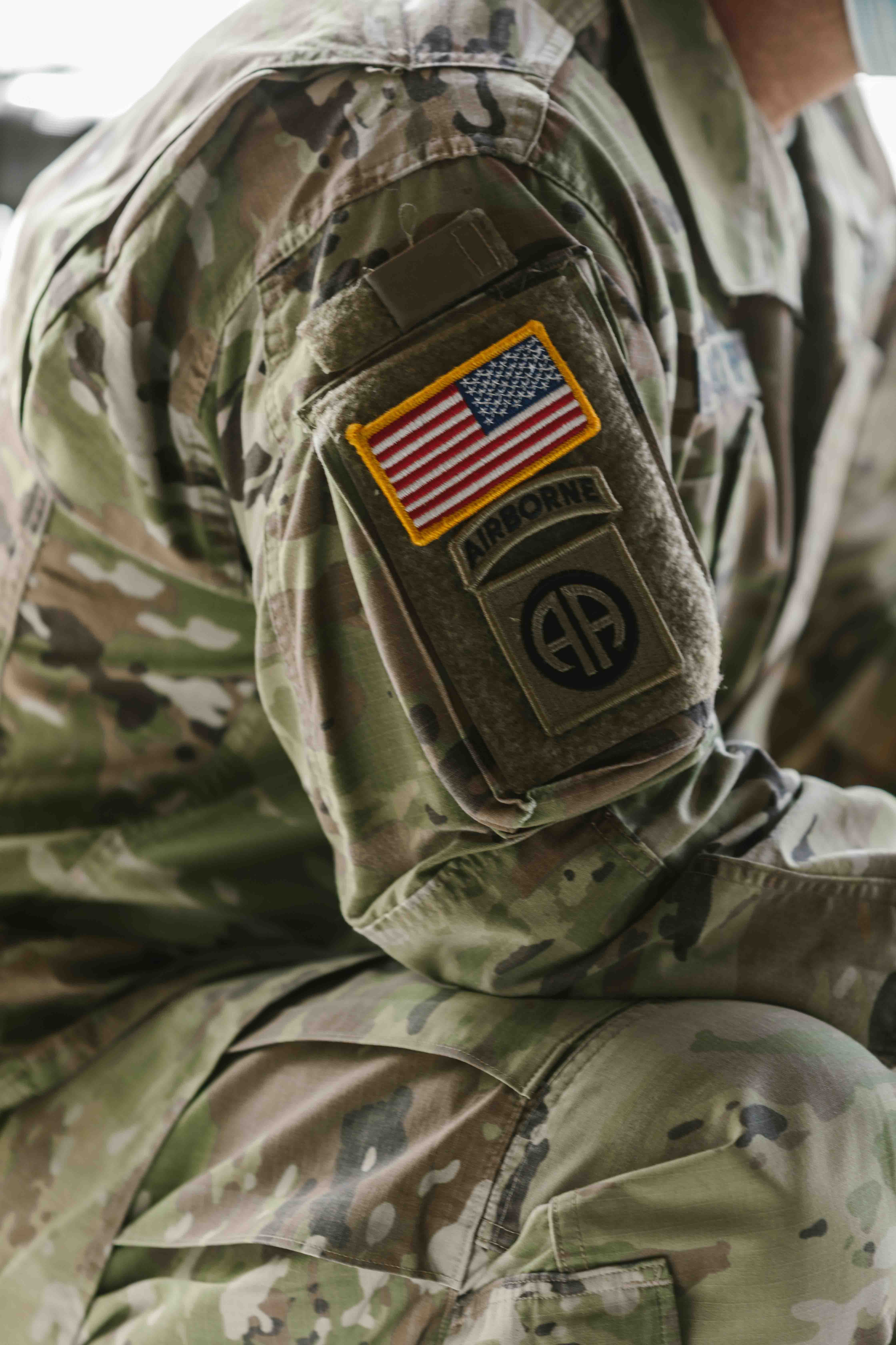 A side shot of a solider sitting shown from the neck to the knee, with arm badges prominently displayed