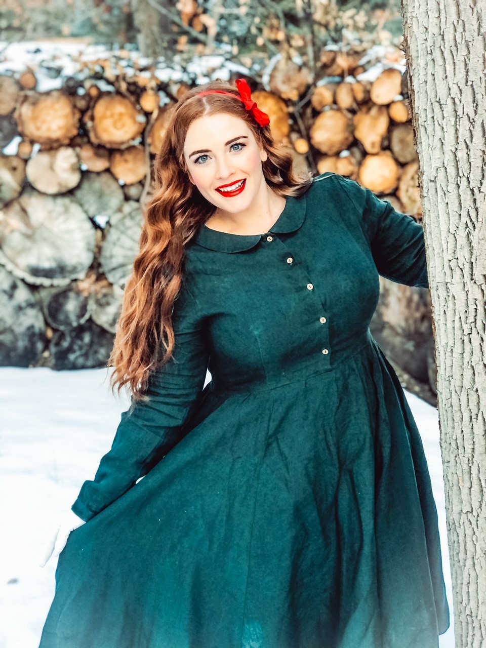 A woman standing outside in winter, leaning out from a tree