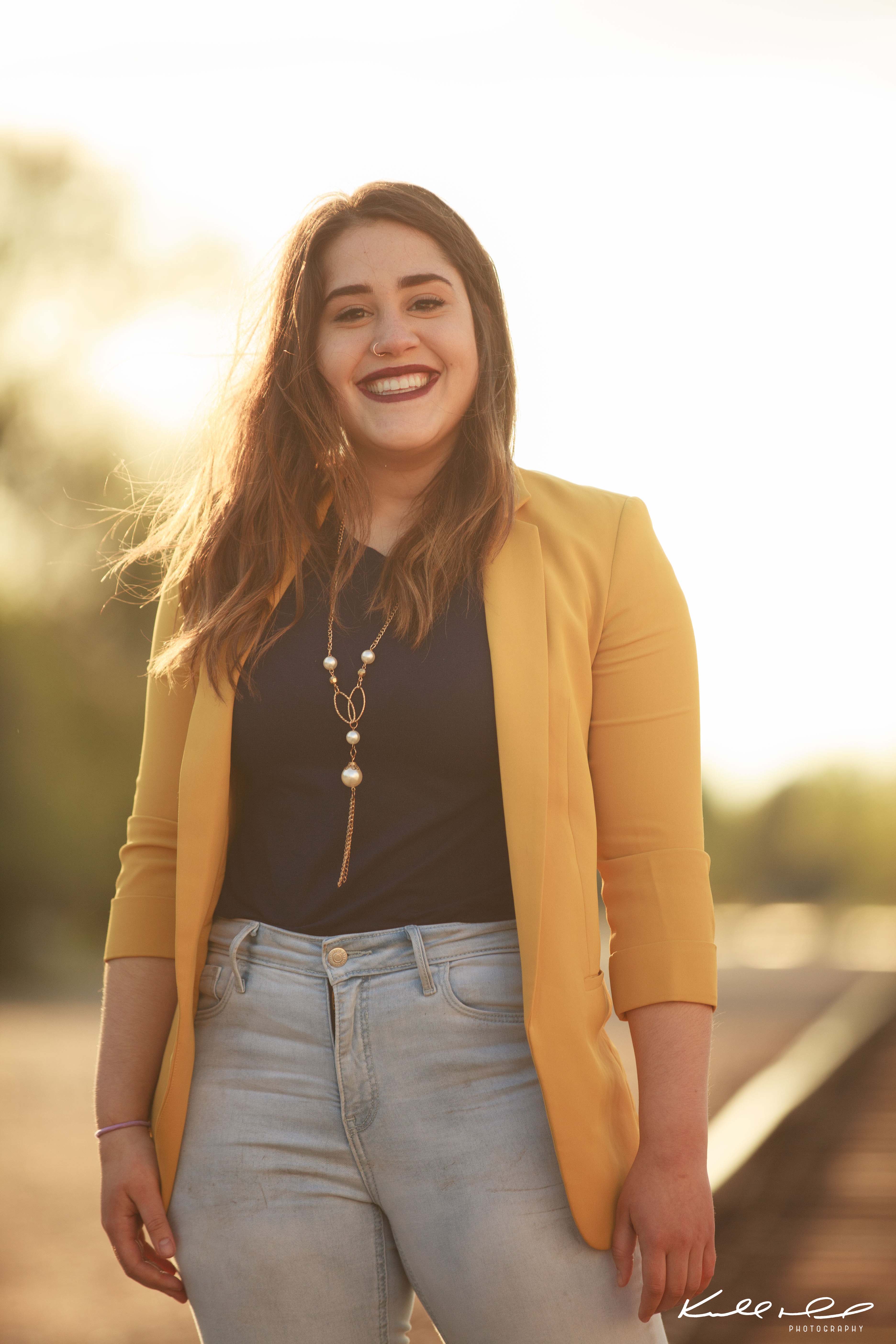 Jessie is standing in the sun and looks at the camera, smiling