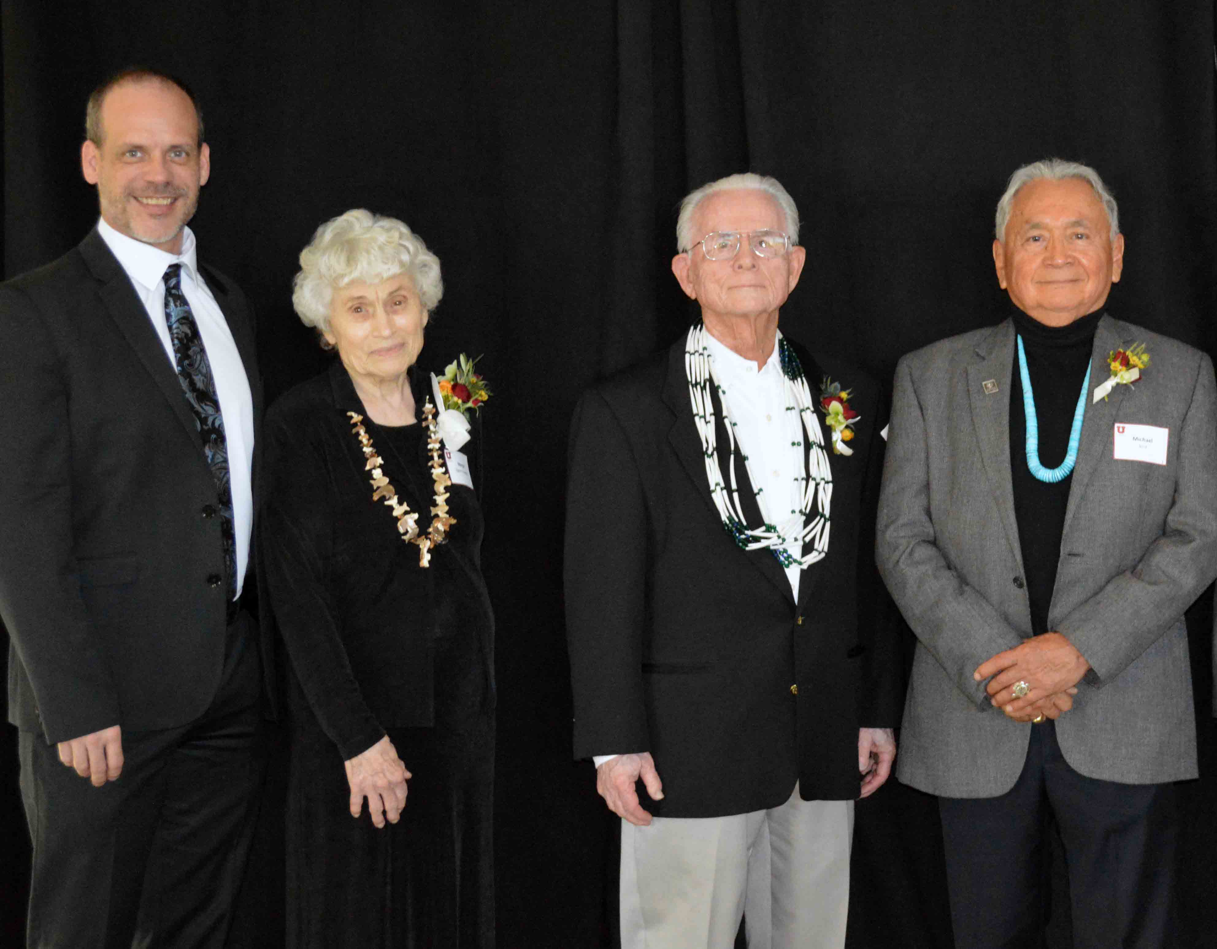 Four middle aged and older adults in semi formal clothing standing in front of a black curtain
