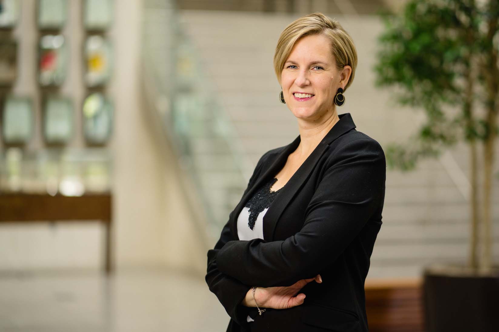 A white woman has her arms folded in front of her and is standing at an angle, looking at the camera