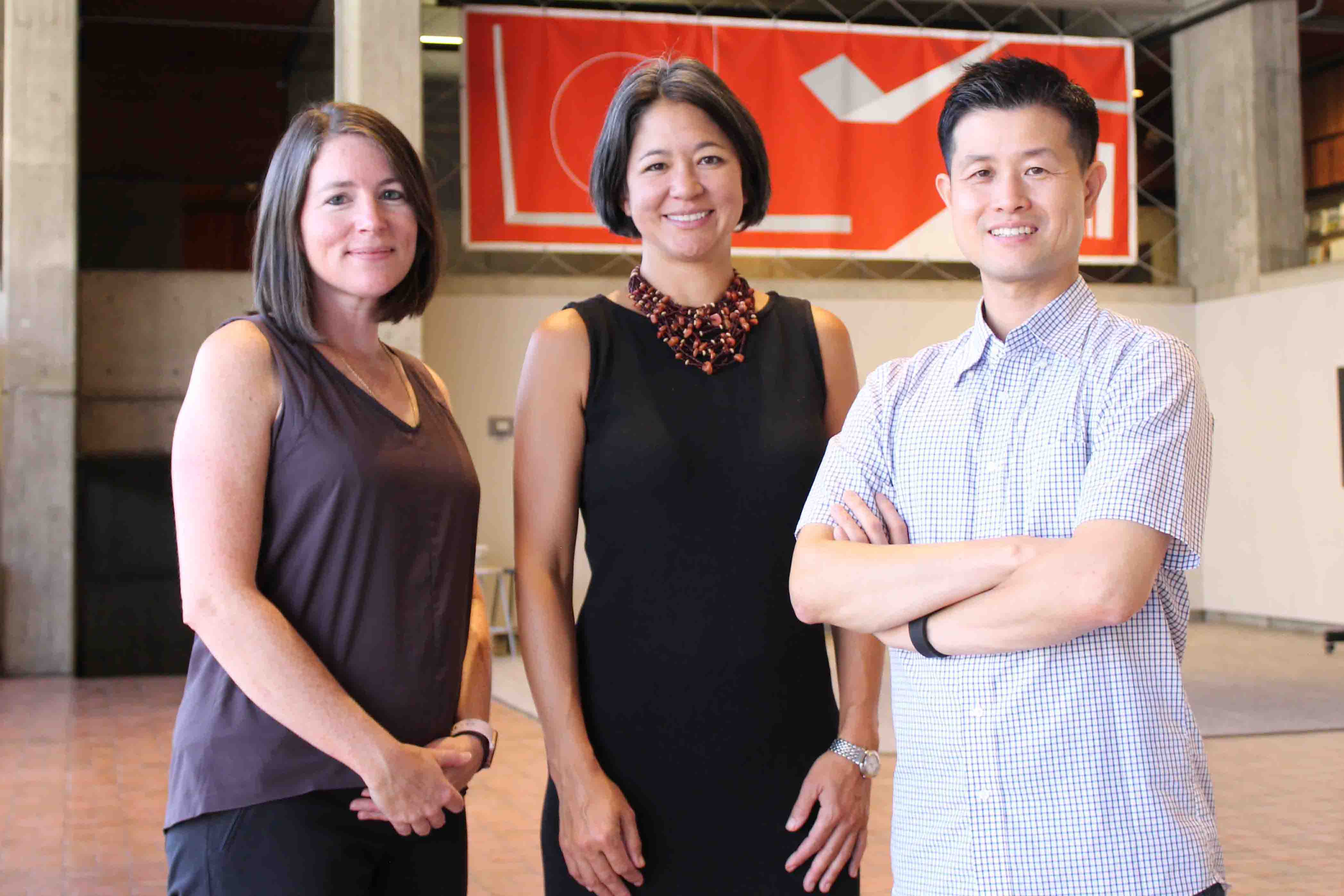 a group shot - three middle age people of differing ethnicities stand side by side in a building lobby