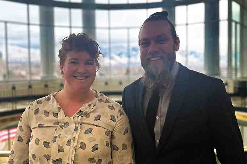 a white woman and white man stand in a rotunda with a window behind them, smiling at the camera