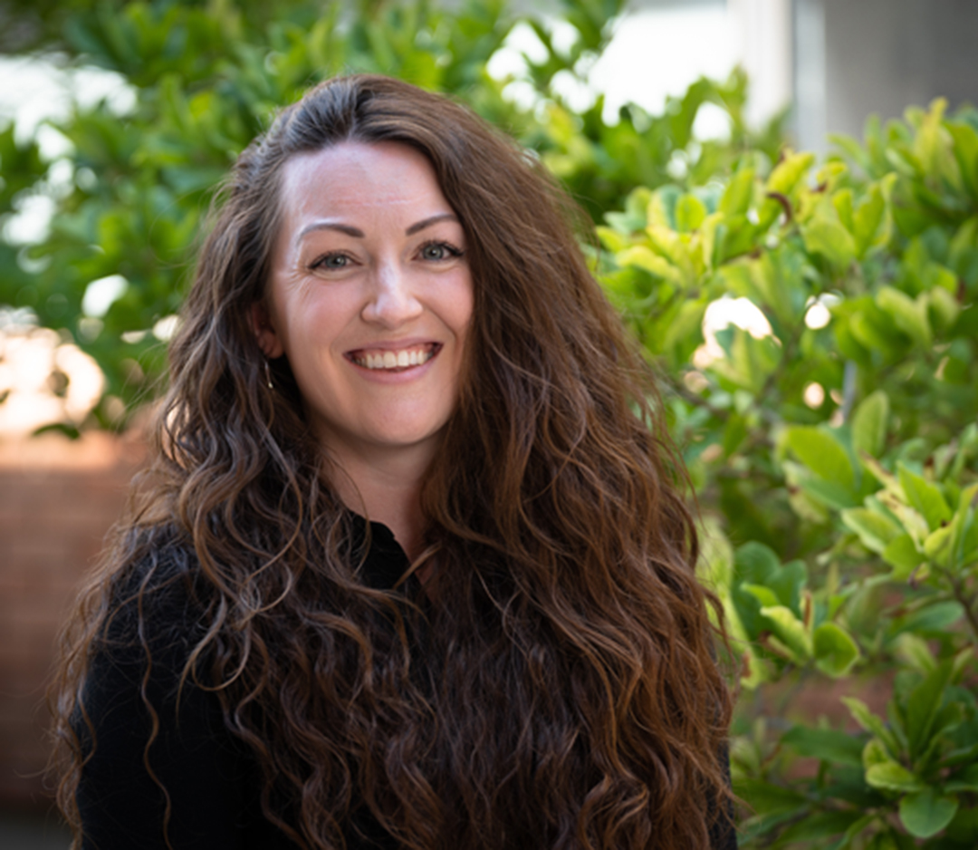 a headshot of Meghan Broadbent smiling in front of a green bush